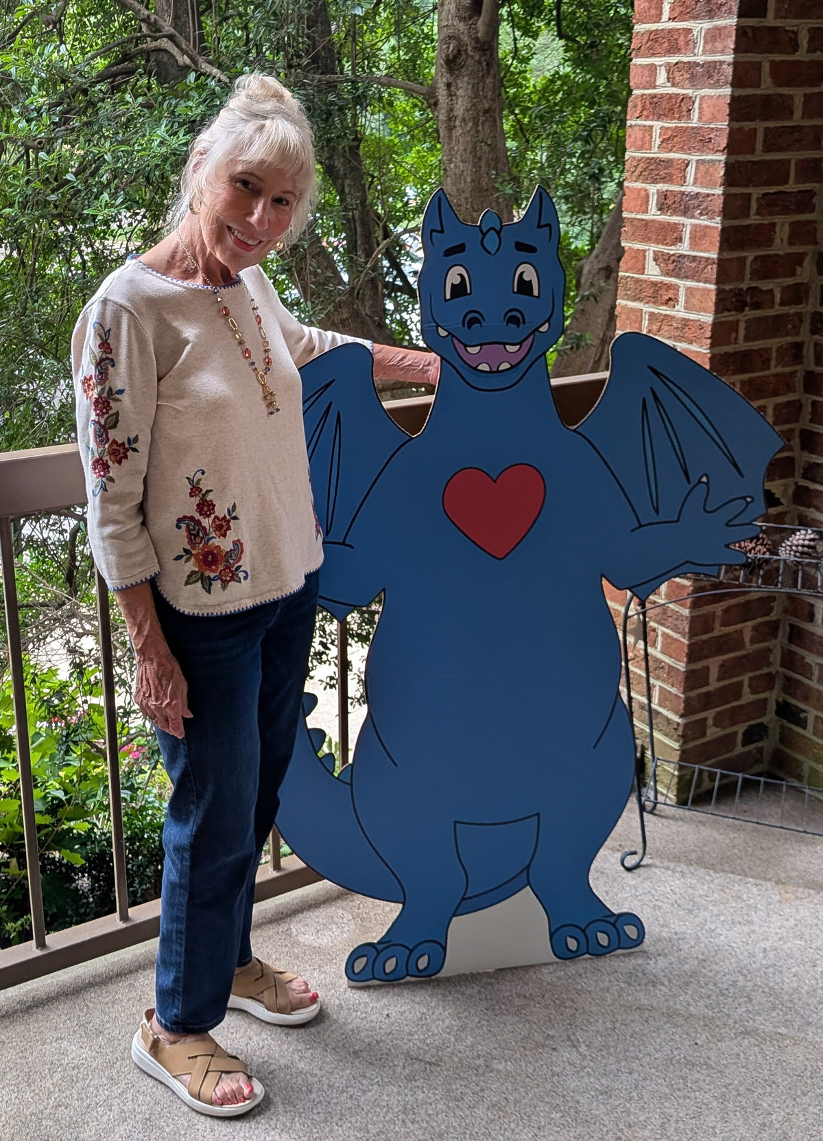 Zobie’s Kids creator Barbara K. Cleary standing beside a life-size cutout of Zobie, the blue dragon with a red heart.